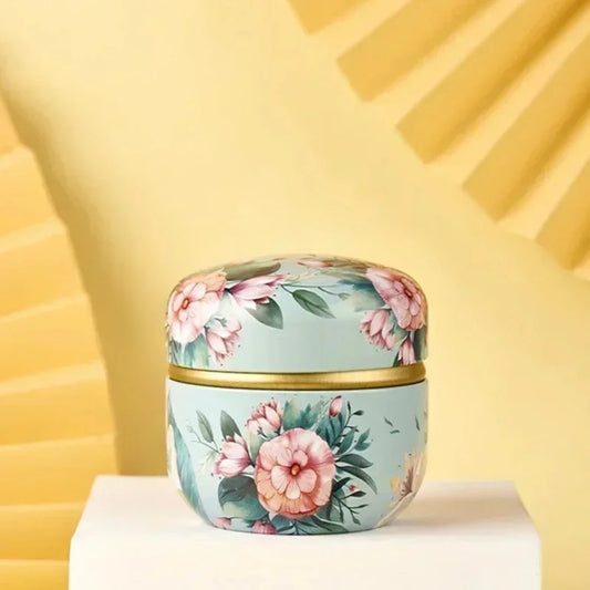 Boîte ronde en métal à décor floral rose et vert sur fond bleu clair, finition élégante et raffinée
