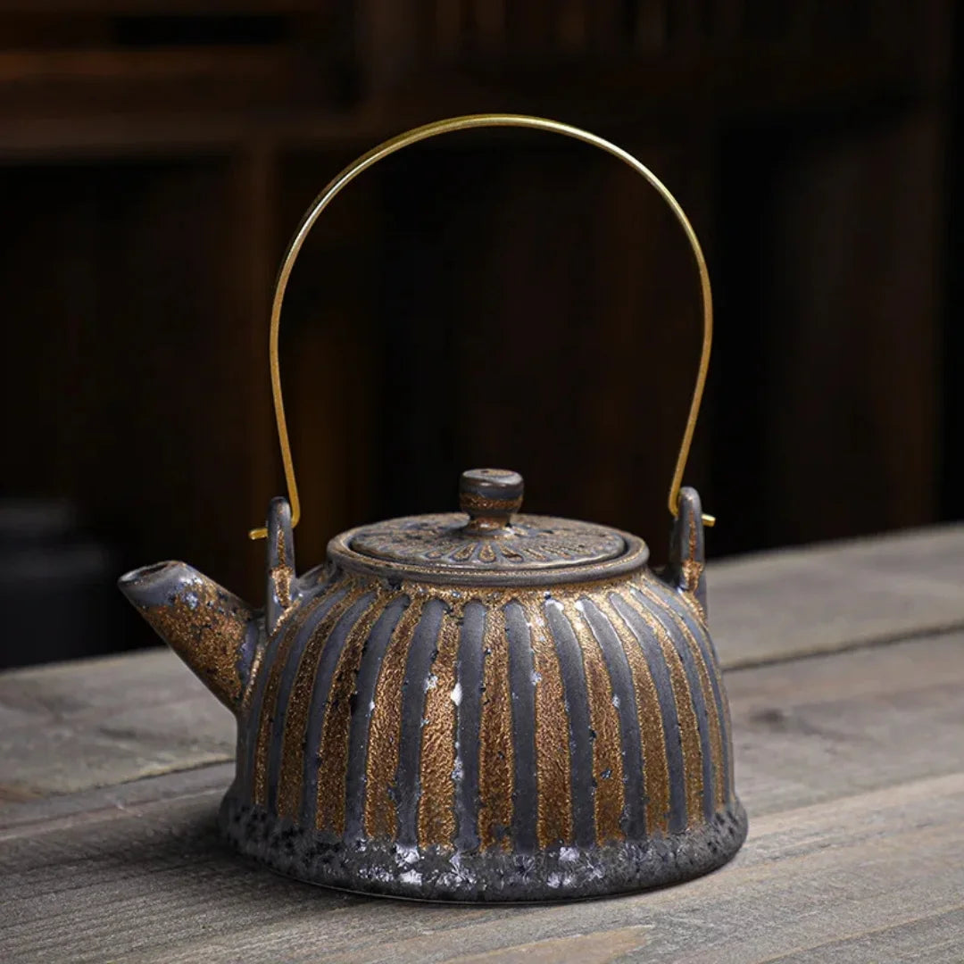 Théière japonaise en céramique sombre à reliefs verticaux, avec anse en laiton, posée sur une table en bois.