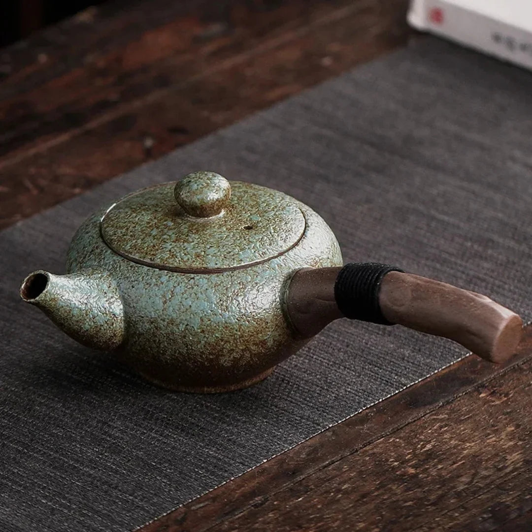 Vue latérale d’une théière japonaise en céramique vert céladon avec poignée latérale en bois.