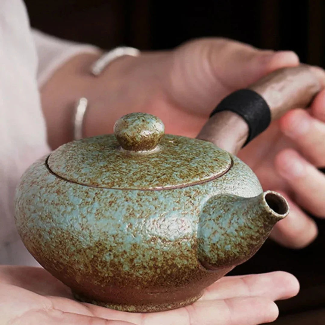 Théière japonaise en céramique vert céladon tenue dans les mains, mettant en valeur sa forme compacte.