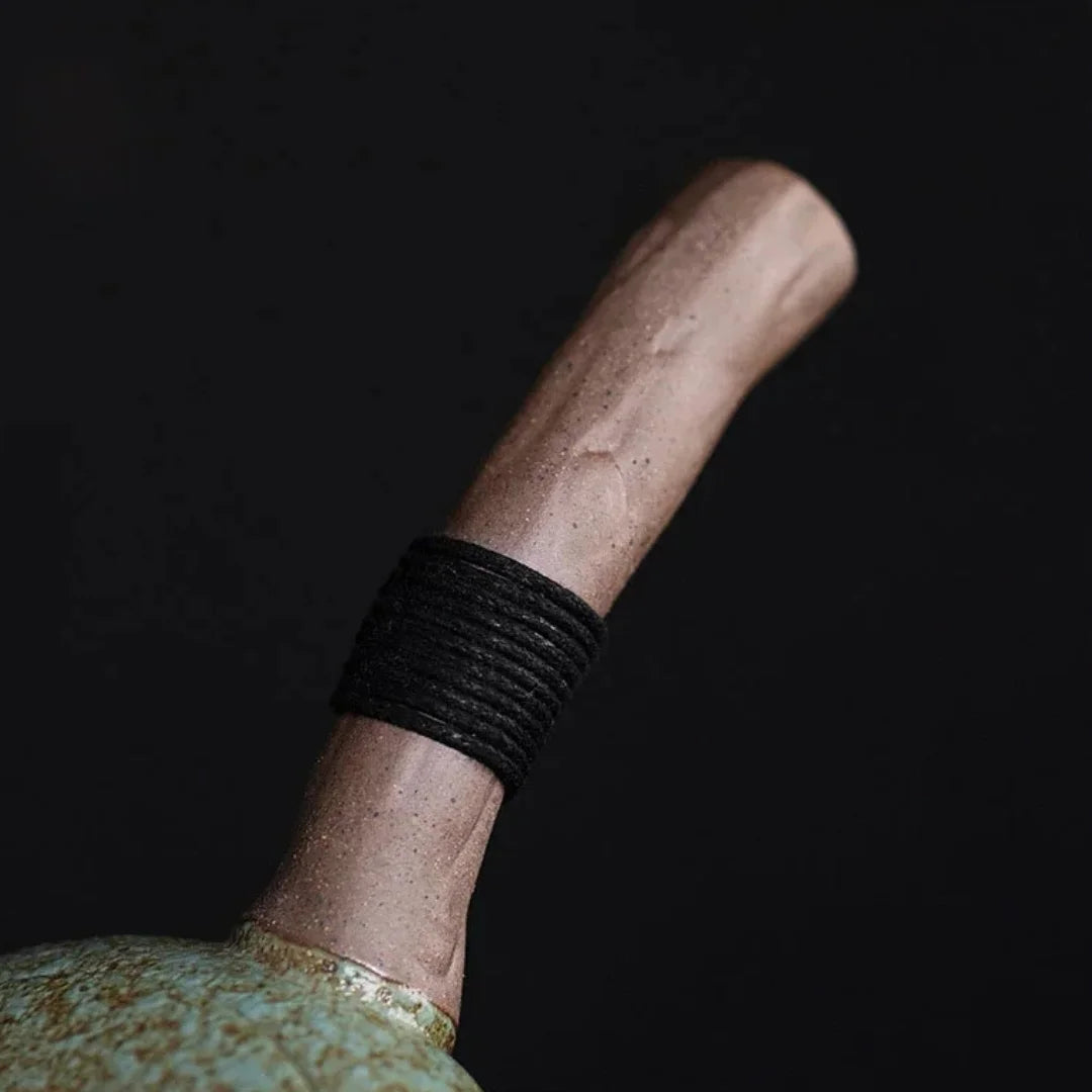 Détail de la poignée latérale en bois d’une théière japonaise, entourée de corde noire.