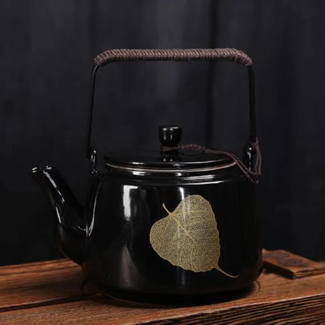 Théière japonaise en métal noir laqué décorée d’un motif feuille dorée, posée sur une table en bois.