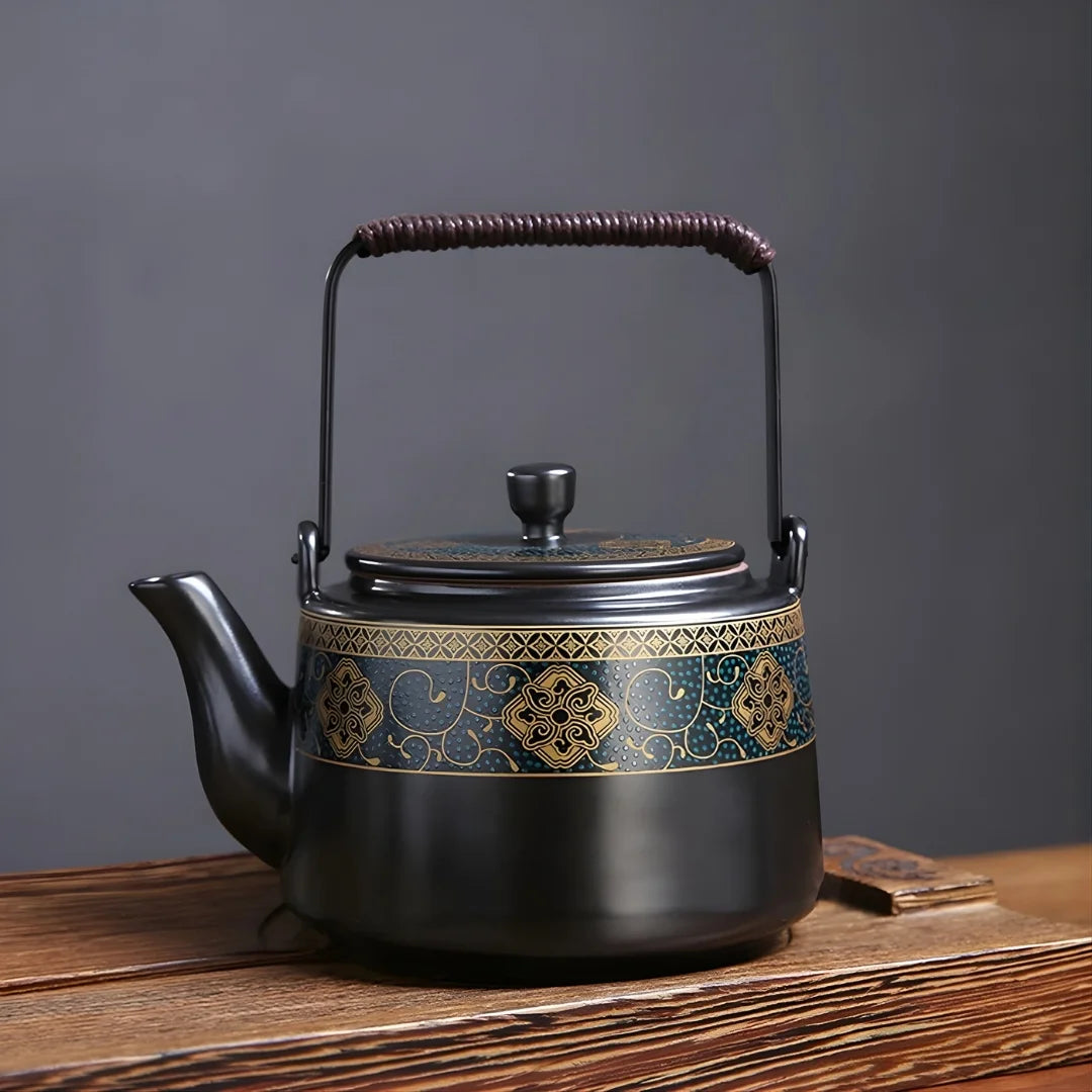 Théière japonaise en métal noir avec frise décorative dorée et bleue, présentée sur une table en bois.