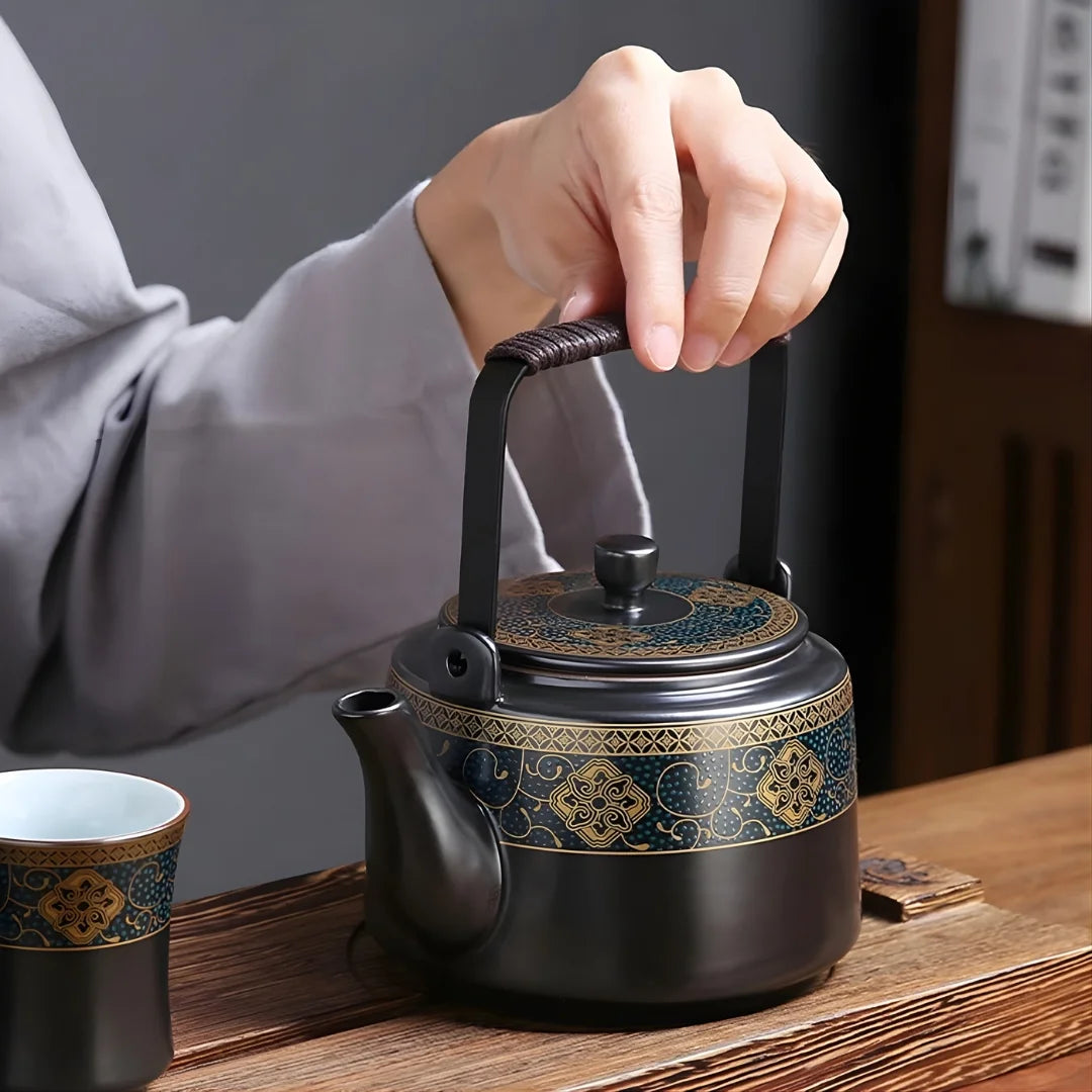 Main tenant l’anse d’une théière japonaise en métal décorée, posée sur une table avec une tasse assortie.