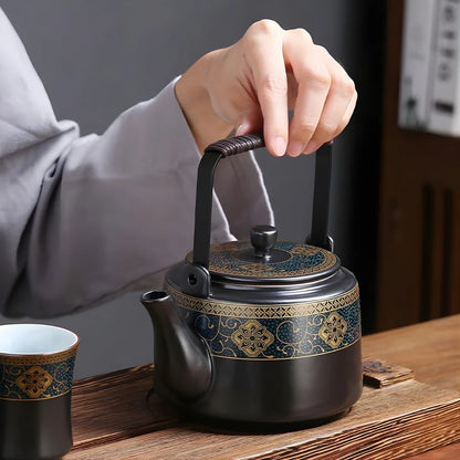 Main tenant l’anse d’une théière japonaise en métal décorée, posée sur une table avec une tasse assortie.