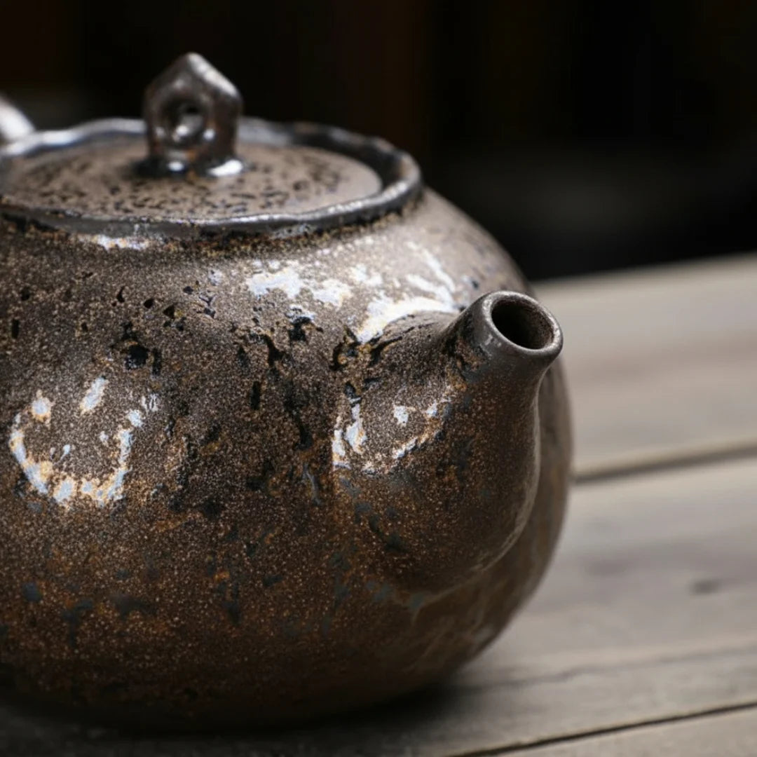 Gros plan sur le bec verseur d’une théière japonaise en céramique à glaçure sombre et minérale.
