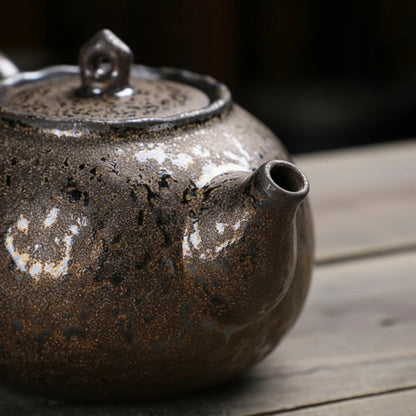 Gros plan sur le bec verseur d’une théière japonaise en céramique à glaçure sombre et minérale.