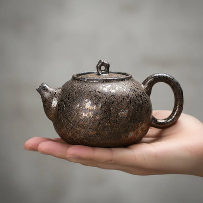 Théière japonaise en céramique sombre présentée dans la paume d’une main, illustrant sa taille compacte.