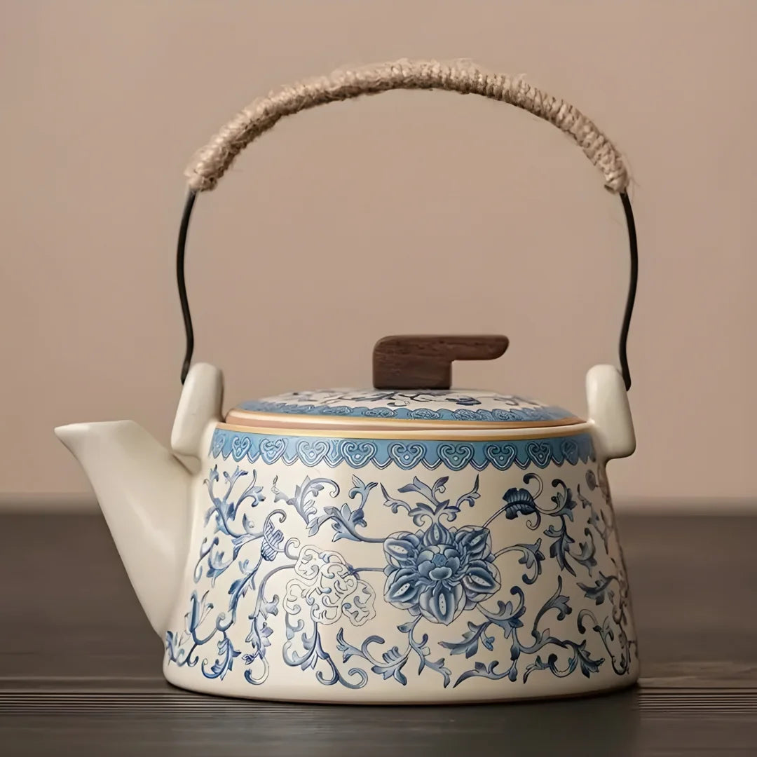 Théière japonaise en céramique blanche décorée de motifs floraux bleus, avec anse en métal gainée de corde et couvercle à bouton en bois.