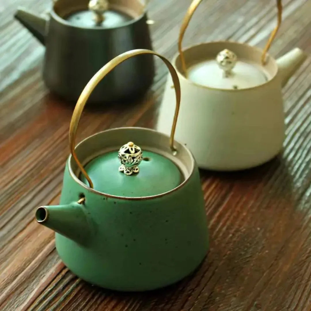 Ensemble de théières artisanales en céramique verte, blanche et noire, alignées sur une surface en bois.