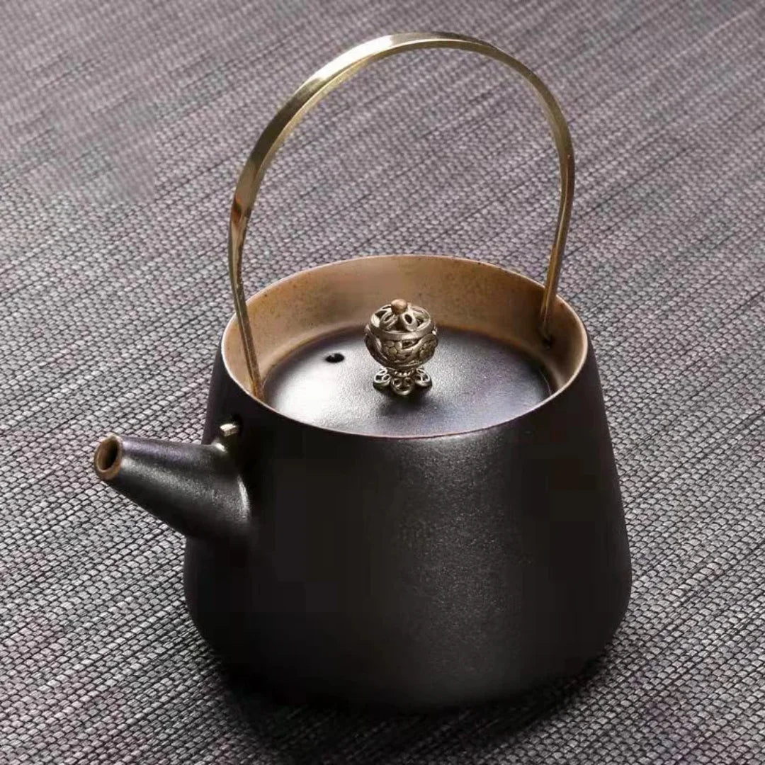 Théière japonaise en céramique noire mate, avec anse en laiton et bouton de couvercle ornemental.