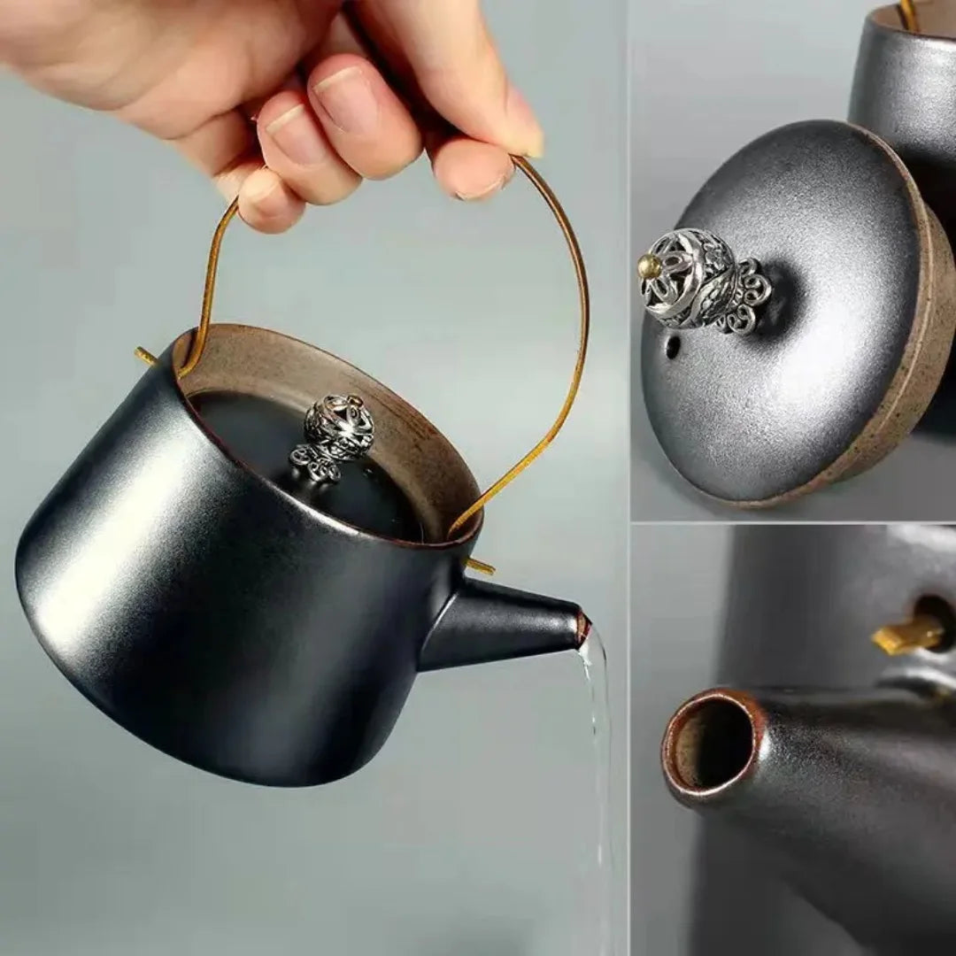 Main versant le thé depuis une théière en céramique noire mate avec anse en laiton.