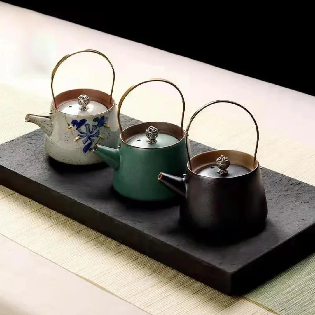Présentation de trois théières japonaises en céramique de différentes couleurs sur un plateau en pierre.