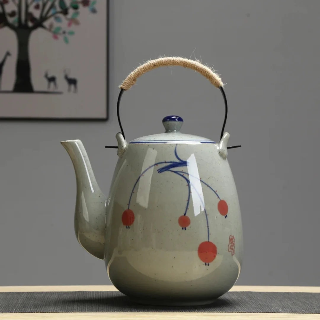 Vue de face d’une théière japonaise en céramique avec décor peint bleu et rouge, posée sur une table.