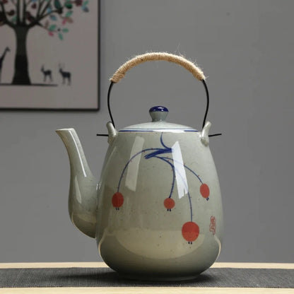 Vue de face d’une théière japonaise en céramique avec décor peint bleu et rouge, posée sur une table.