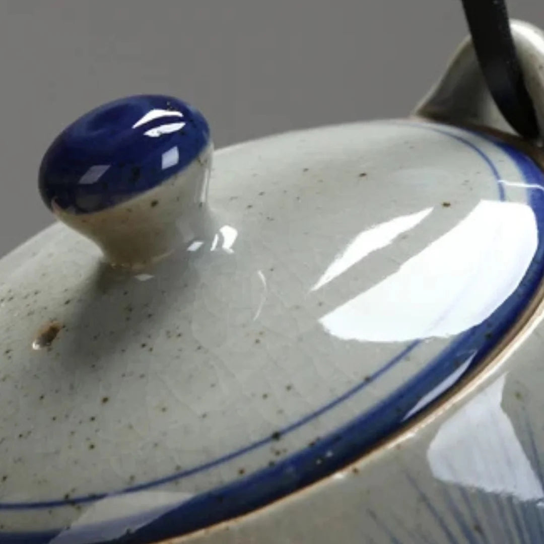 Gros plan sur le couvercle d’une théière japonaise en céramique, bouton bleu émaillé et liseré peint.
