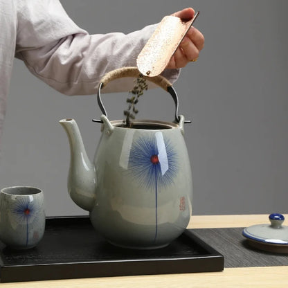 Personne versant des feuilles de thé dans une théière japonaise en céramique décorée.
