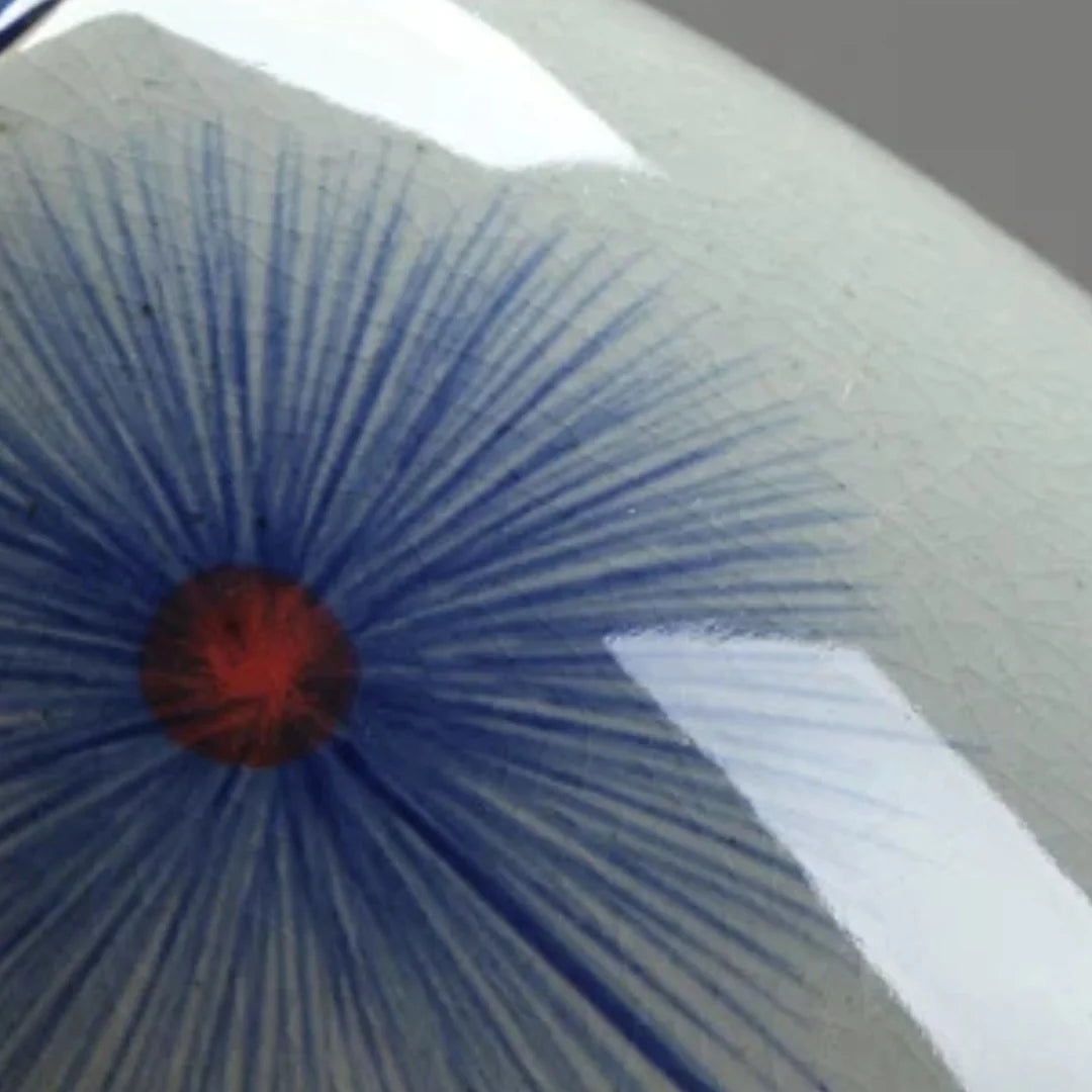 Gros plan sur un motif peint bleu en éventail avec centre rouge, sur une théière japonaise en céramique émaillée gris clair.
