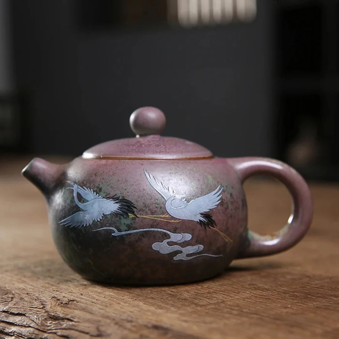 Théière japonaise en céramique artisanale, décorée de grues blanches en vol sur fond patiné vert et brun.