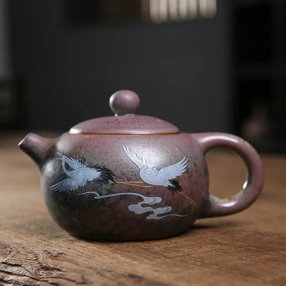 Théière japonaise en céramique artisanale, décorée de grues blanches en vol sur fond patiné vert et brun.