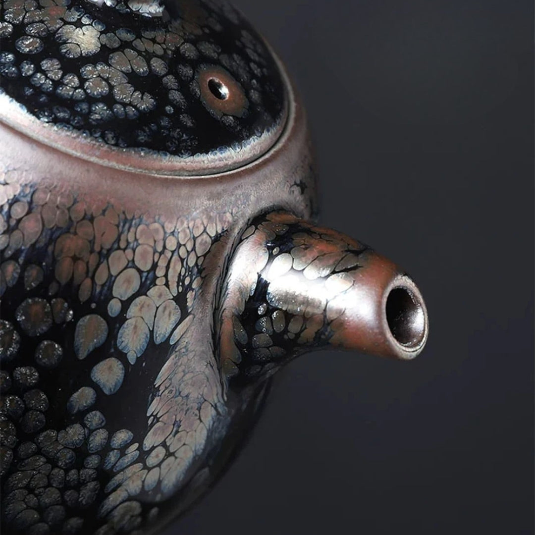 Gros plan du bec verseur d’une théière japonaise à glaçure cristallisée noire et reflets métalliques.